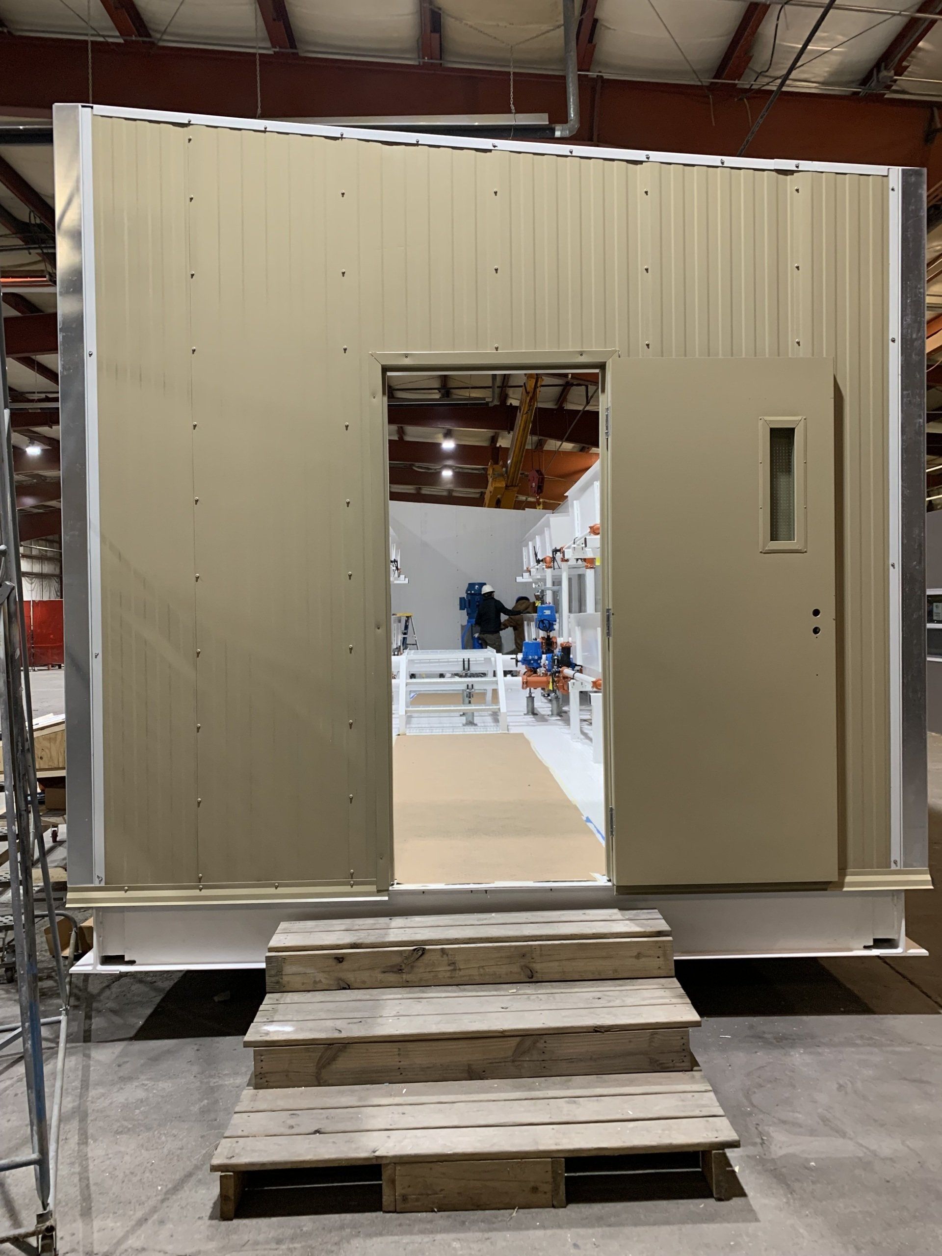 Temporary beige modular building with open doorway and ramp made of stacked pallets leading to the entrance