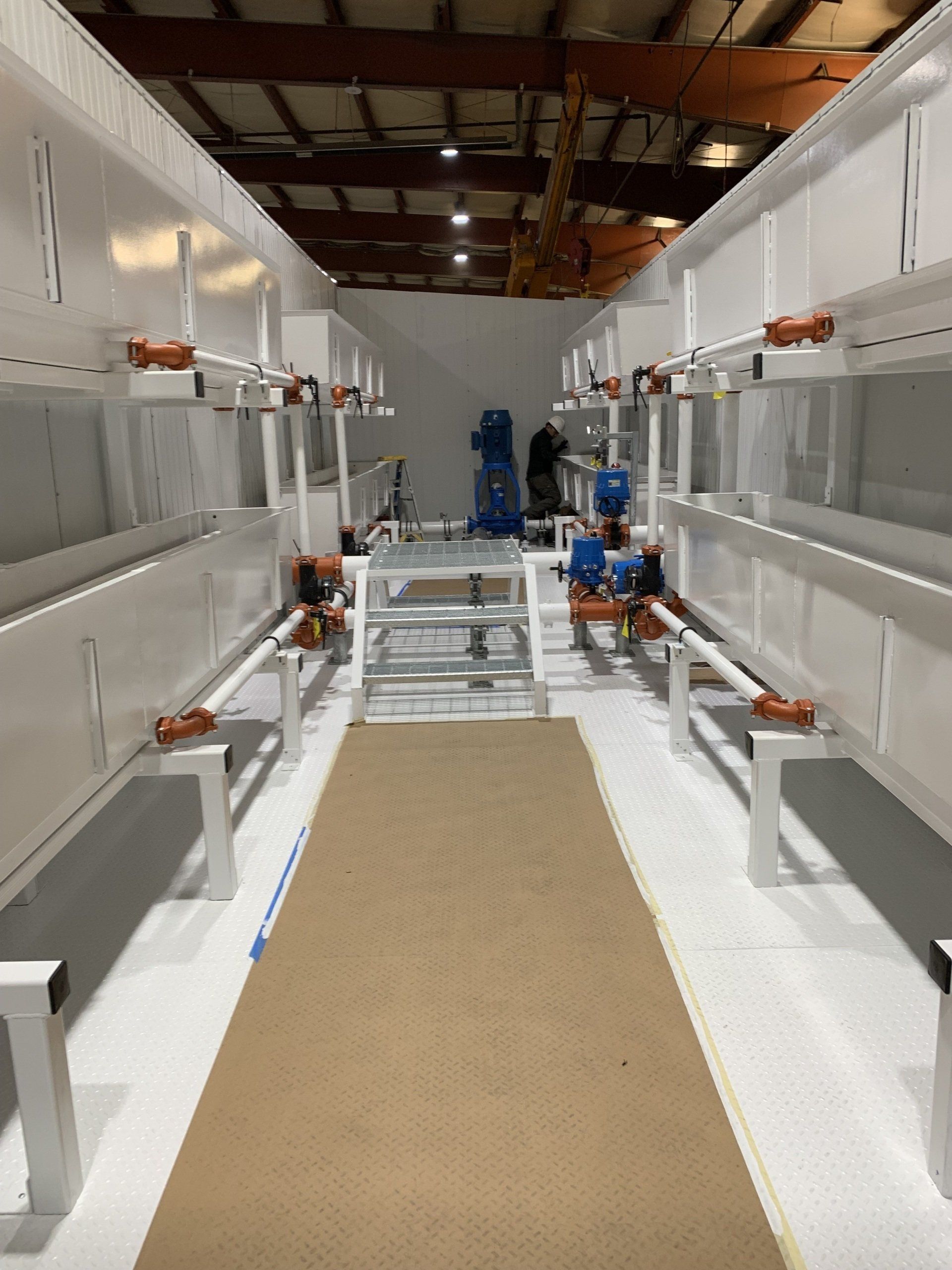 Long narrow industrial aisle with white benches, a tan floor runner, and equipment at the far end
