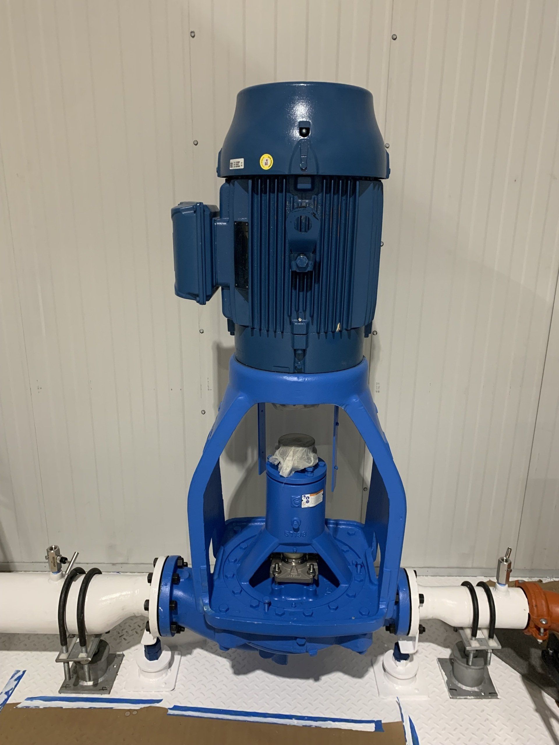 Blue industrial motor mounted on white piping against a beige wall
