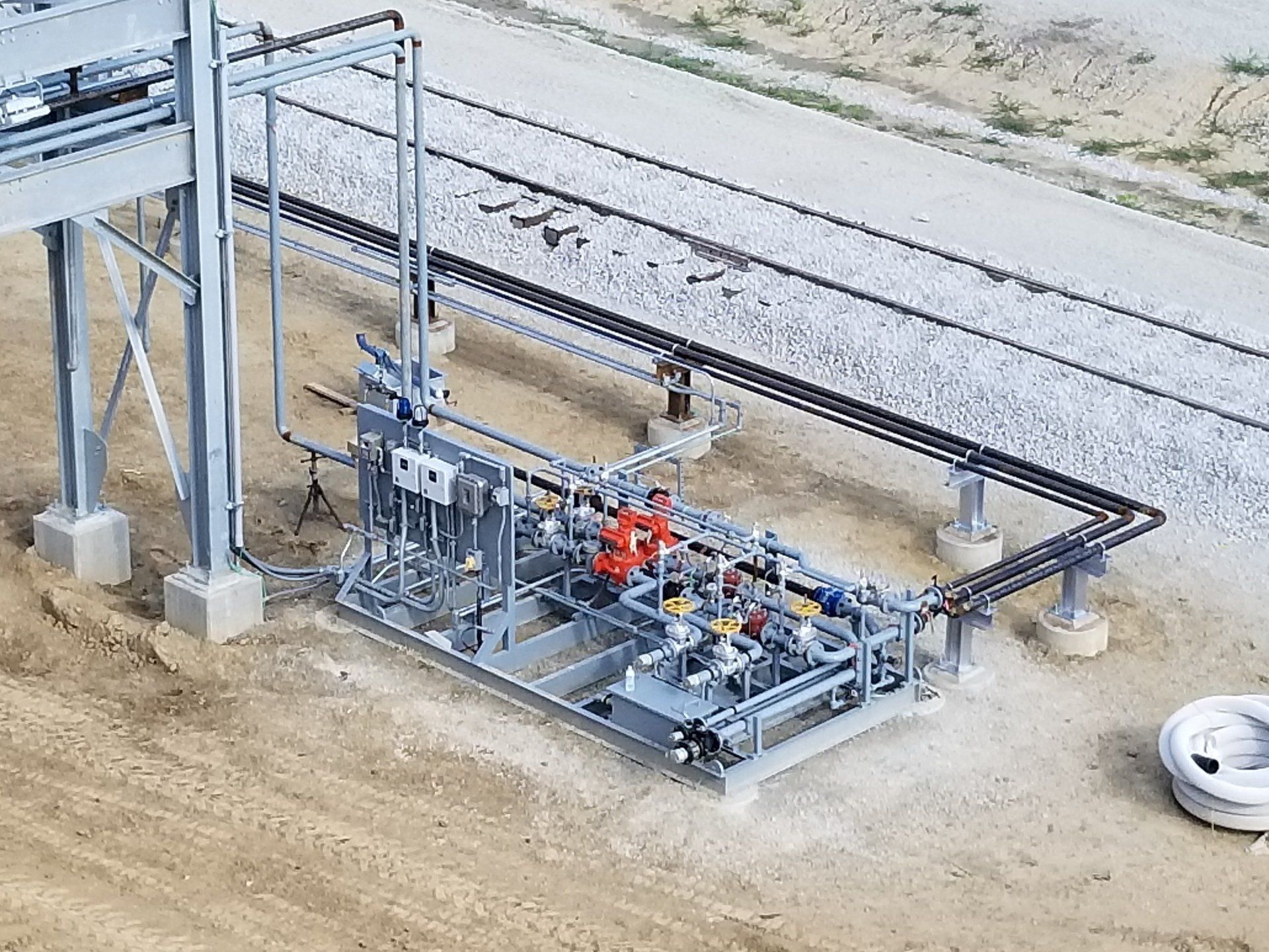 Industrial railway equipment beside tracks, with a red machine and metal framework on a concrete pad.