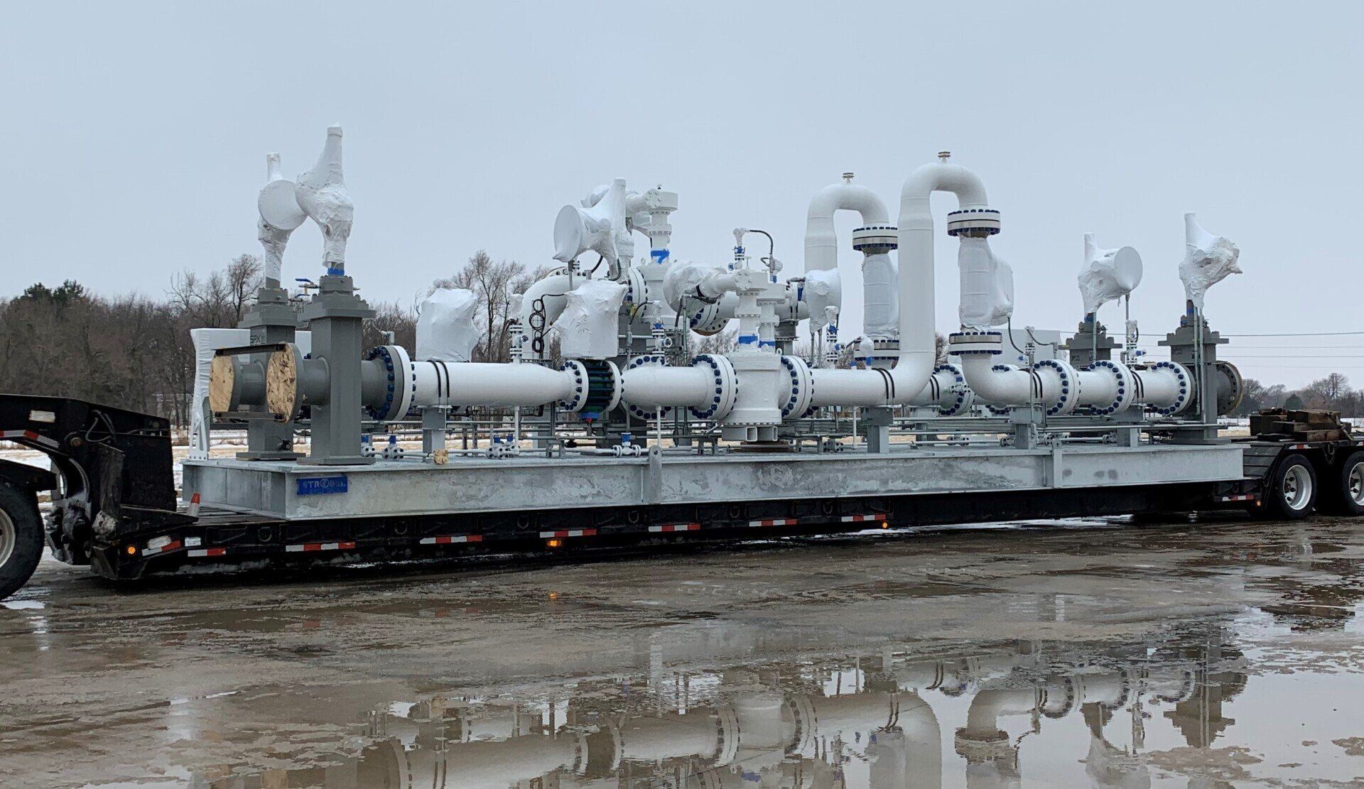 Large industrial gas processing unit mounted on a trailer in a muddy outdoor yard