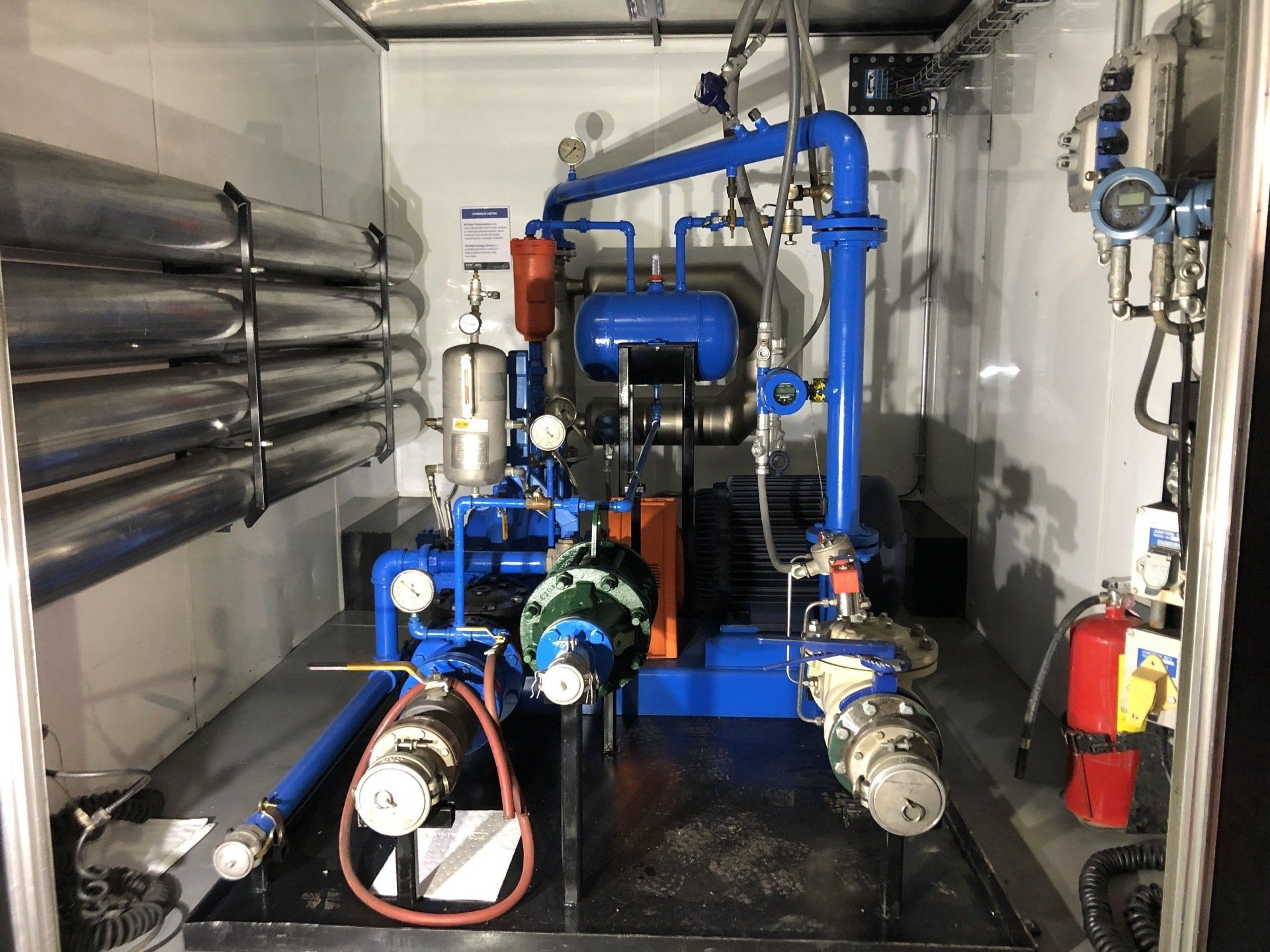 Industrial pump and piping system in a mechanical room with blue and silver equipment.