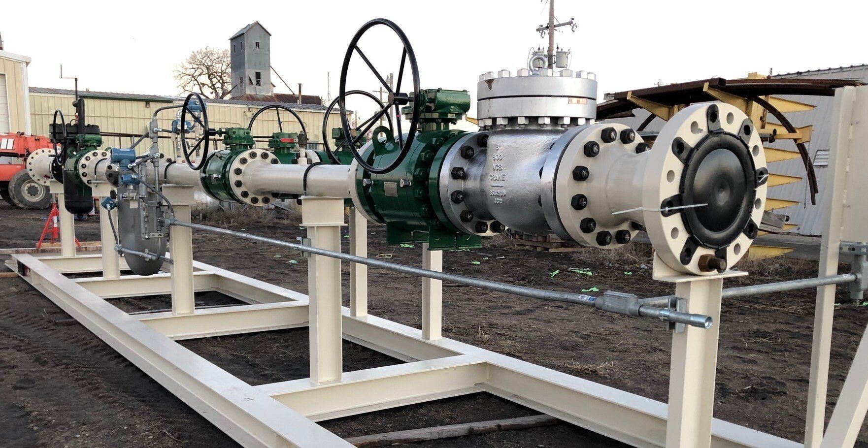 Industrial pipeline and valve assembly on white metal supports in an outdoor facility.