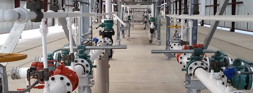 Industrial piping and valves on a factory walkway, with white pipes and colored valve handles.