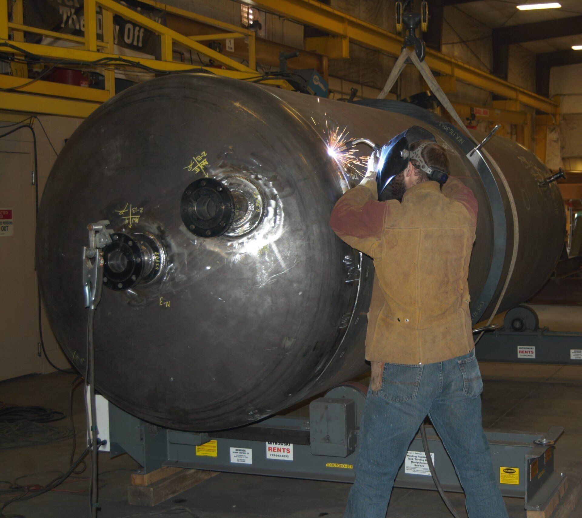 Worker welding a large black industrial tank in a factory workshop