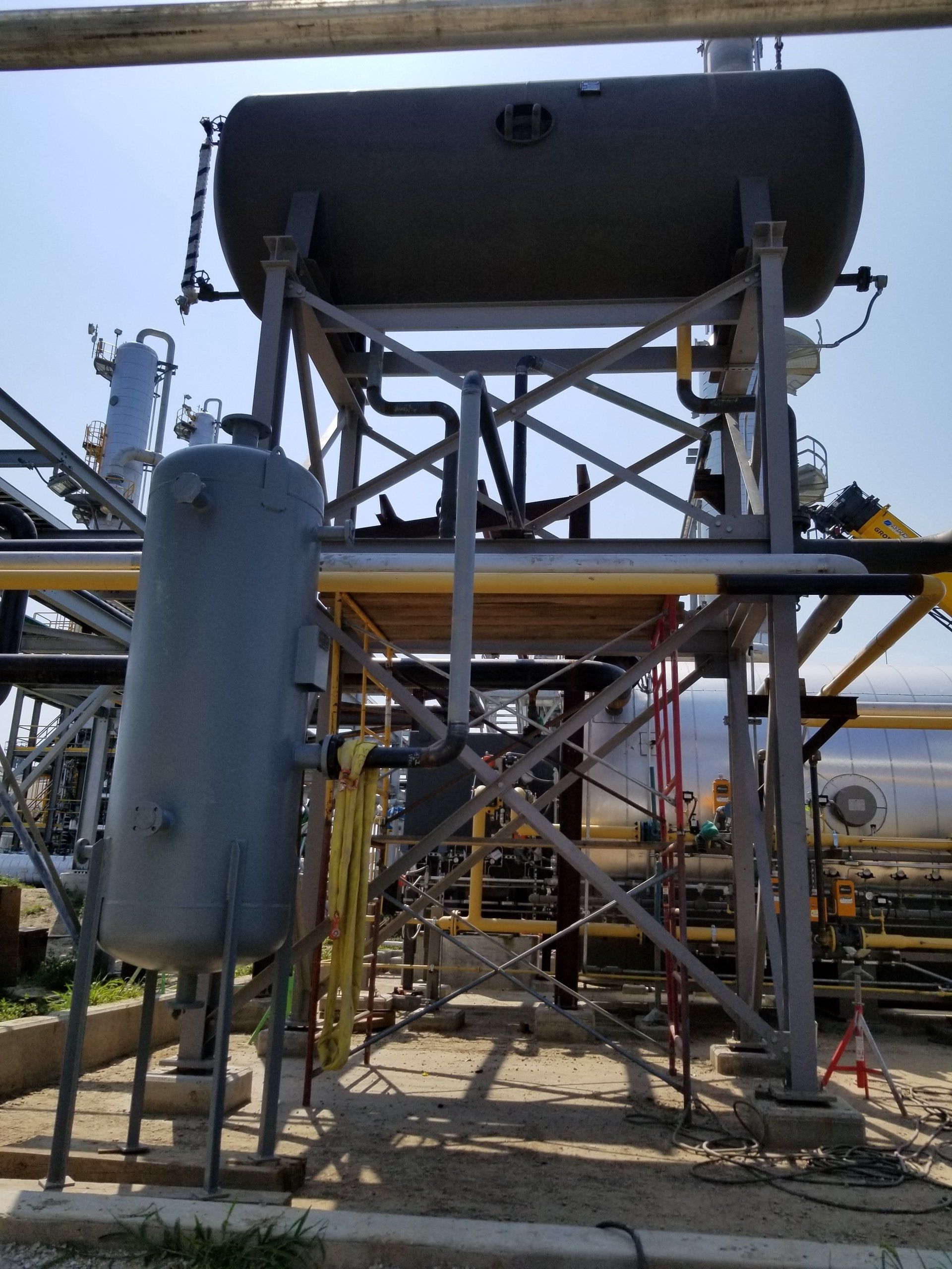 Industrial plant equipment with large black tank and metal framework against an outdoor sky.