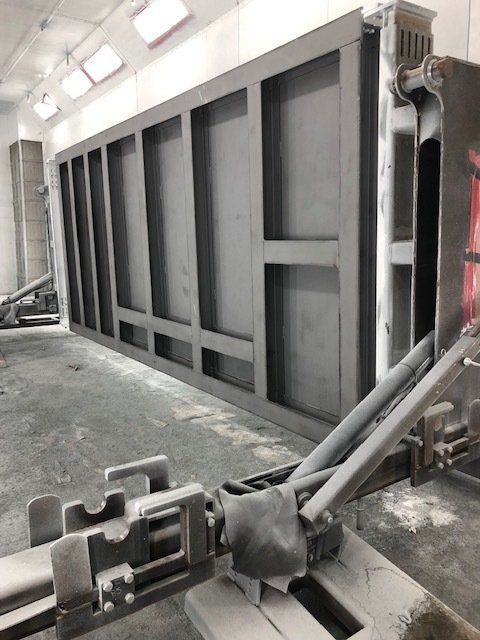 Large gray industrial machine in a workshop with metal pipes and a concrete floor