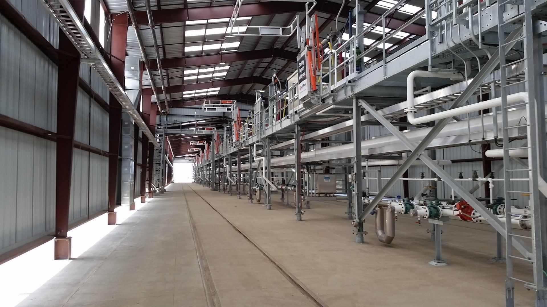 Industrial warehouse interior with metal shelving, red steel beams, and a long empty concrete aisle