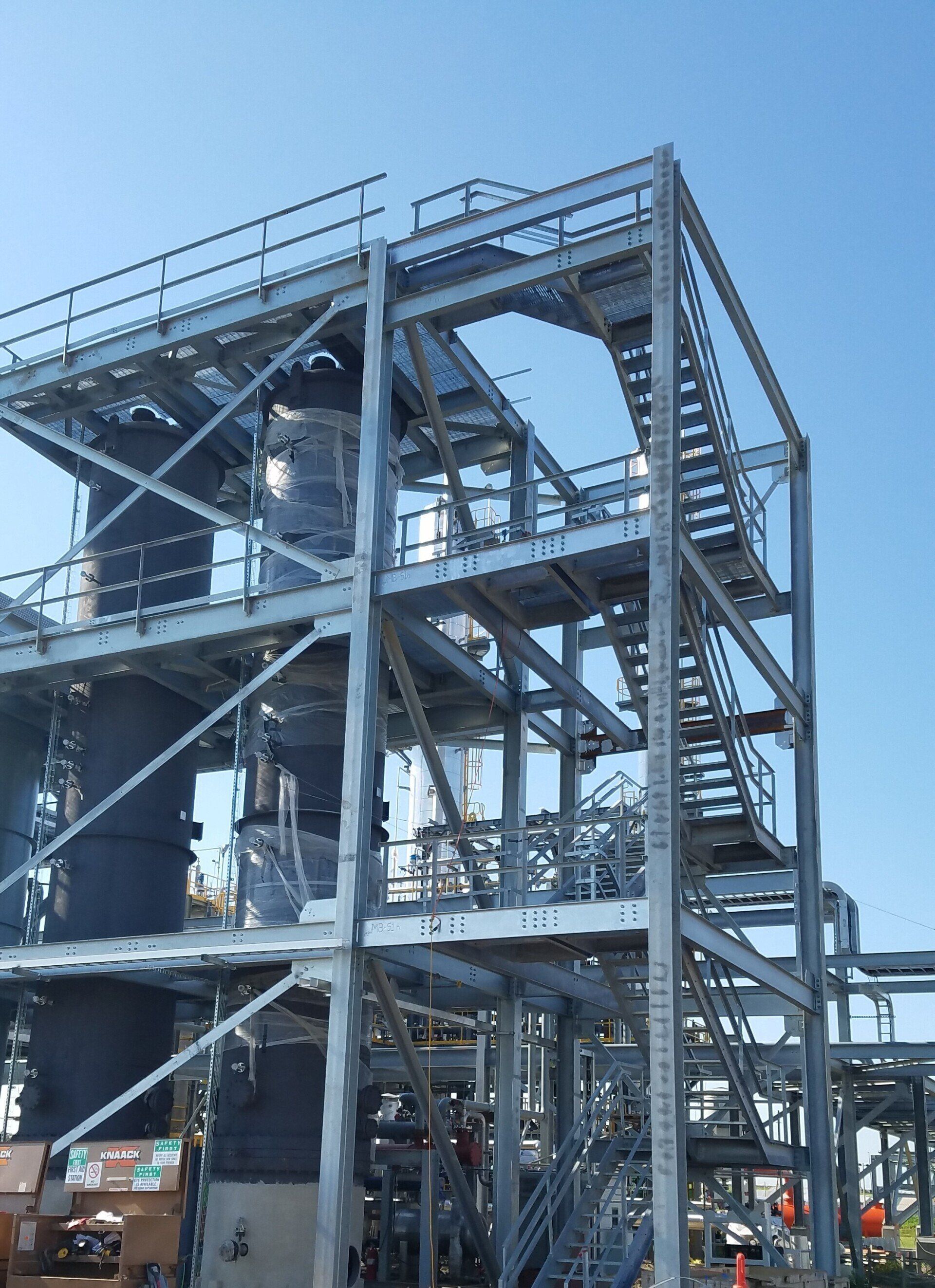 Industrial steel framework with staircases and platforms under a clear blue sky