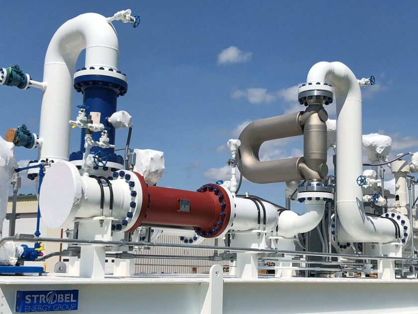Industrial piping and valves at a plant, with large white pipes and a red cylindrical component against a blue sky