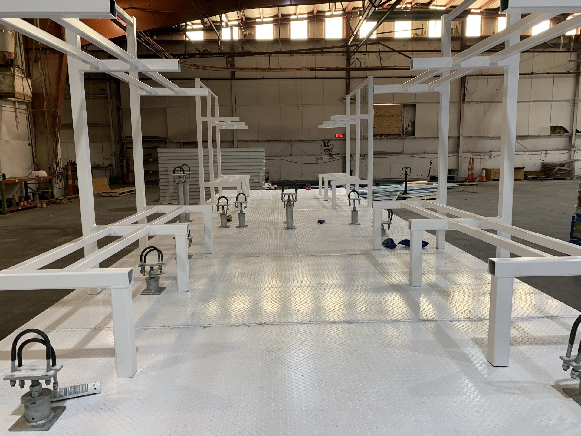 Indoor warehouse with white metal frames and equipment on a glossy floor under skylights.