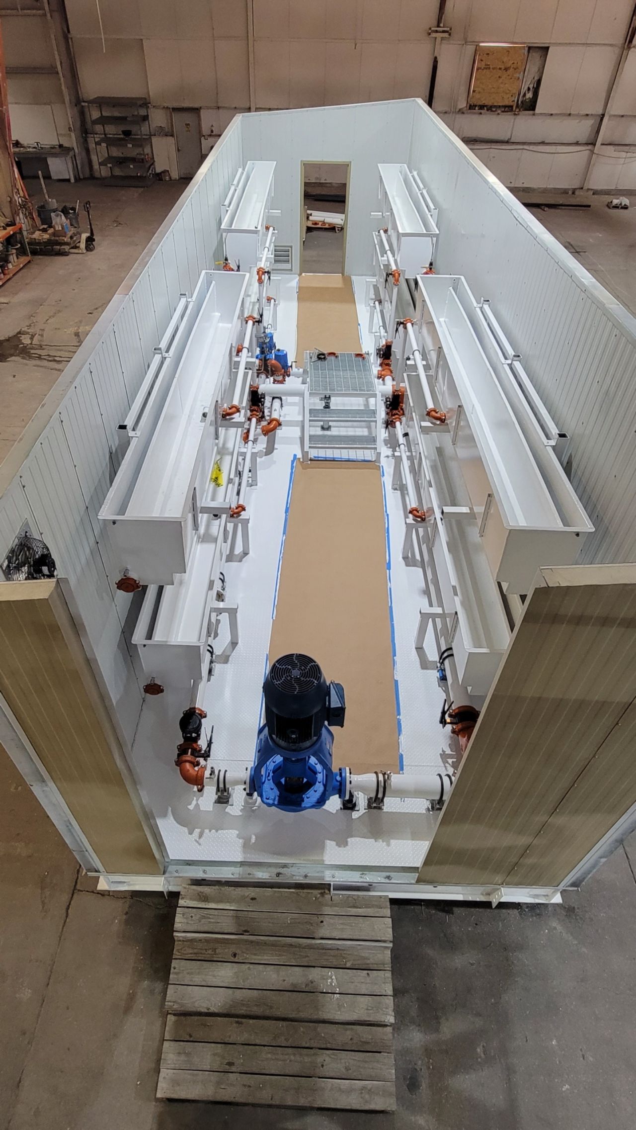 Indoor industrial hall with a long white equipment assembly line and a large blue machine in the foreground.