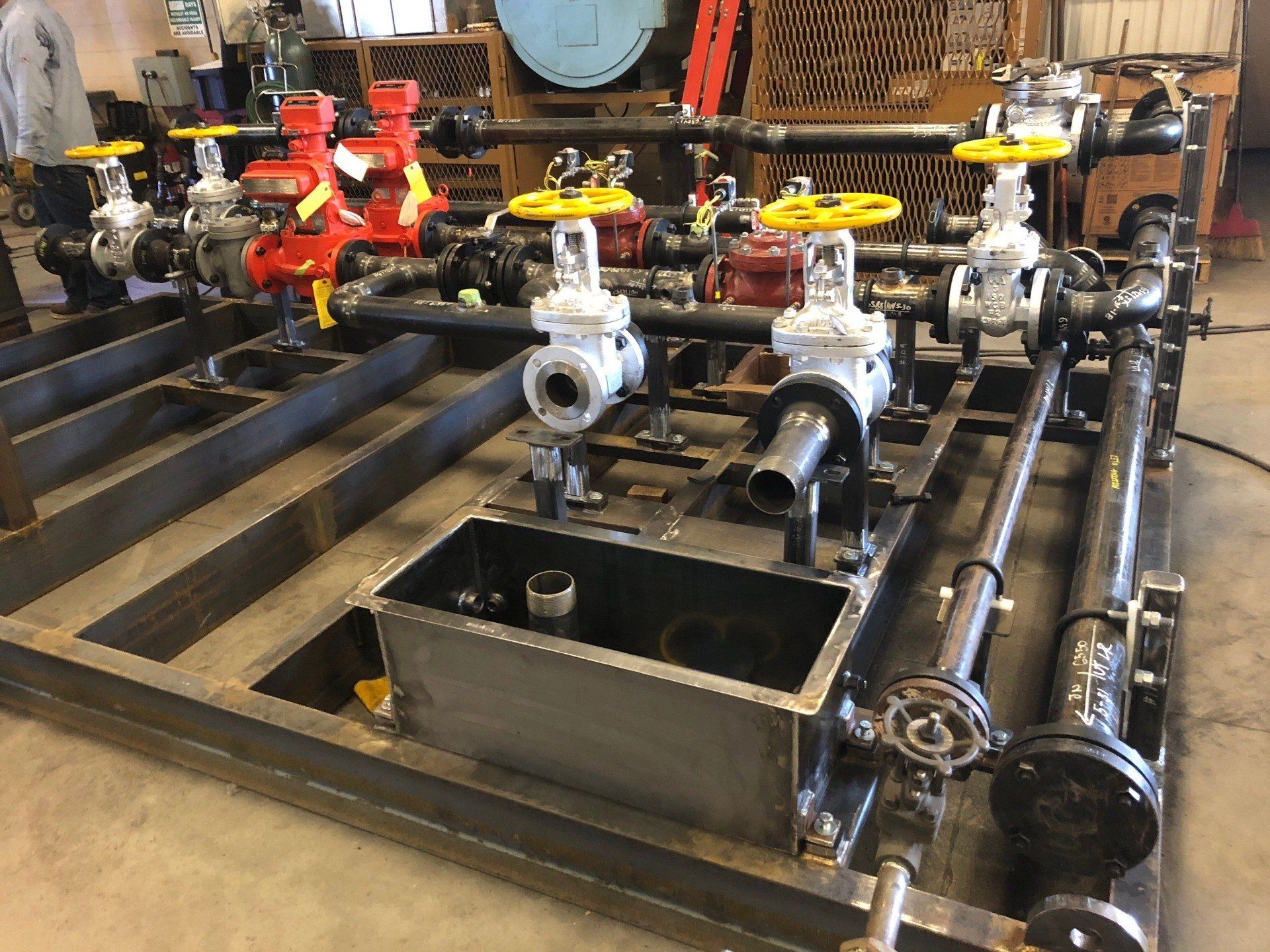 Industrial pump and valve assembly with red, yellow, and white handwheel valves on black piping.