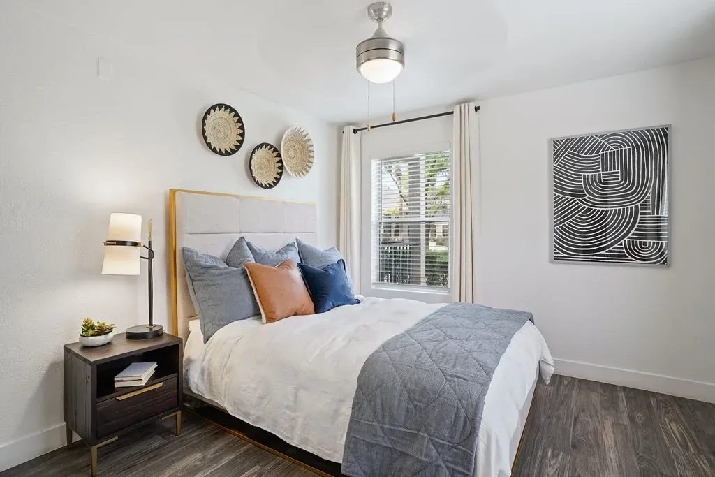Bedroom with a large bed, nightstand, window, and abstract wall art.