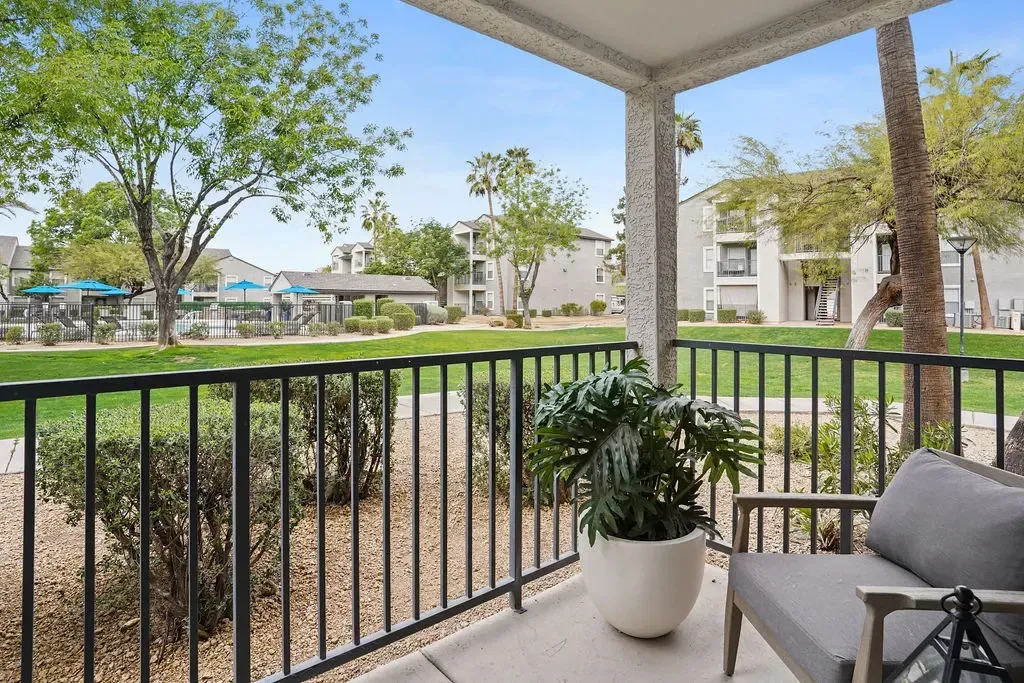 Balcony view with a potted plant and chair overlooking a landscaped community lawn and pool.