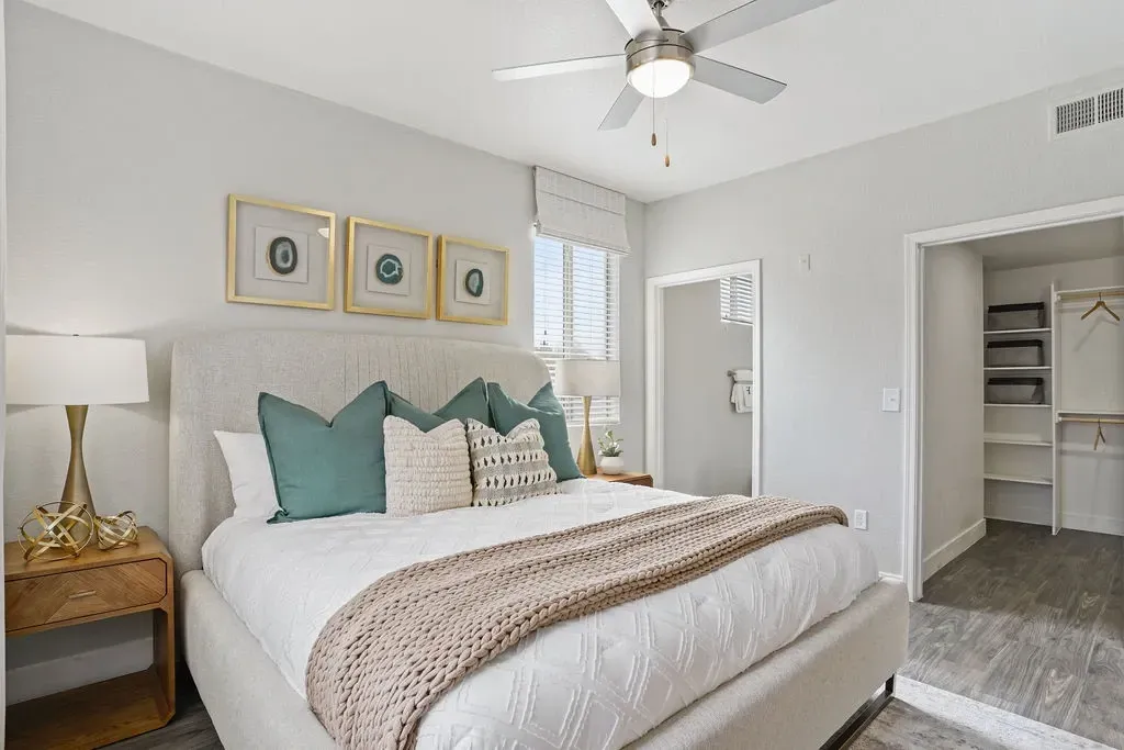 Bedroom in an apartment with padded headboard bed, nightstands, ceiling fan, and open closet.