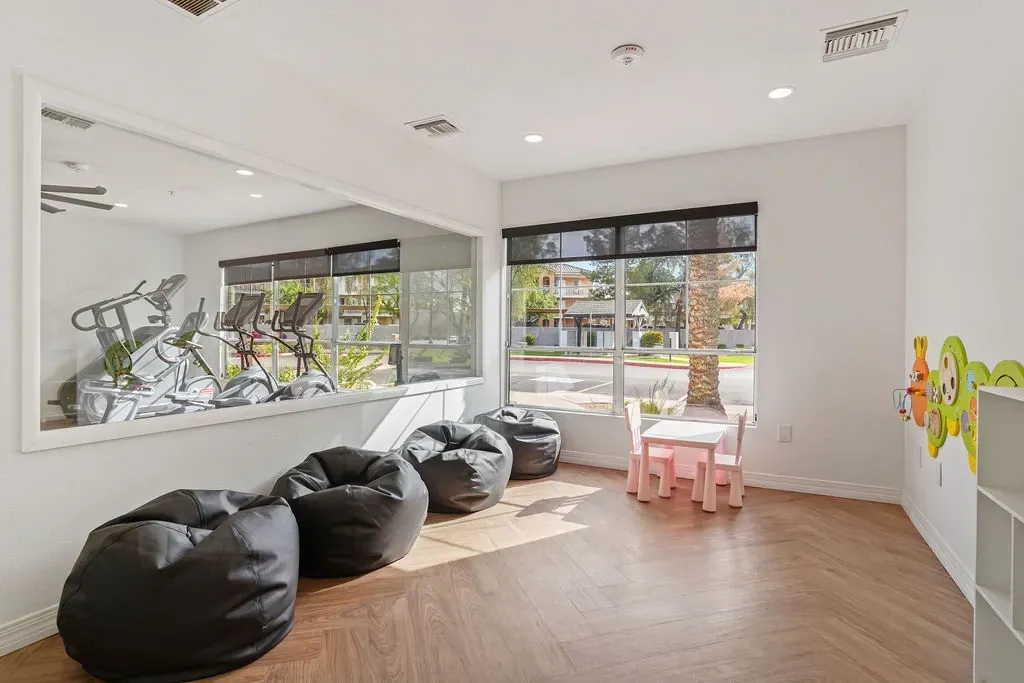 Bright community room with exercise equipment visible through window and a small kids' play area.