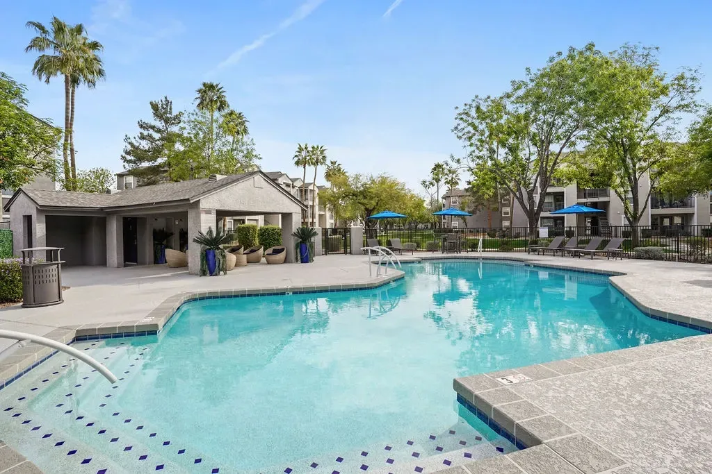 Outdoor pool at a multifamily community with lounge chairs and blue umbrellas.