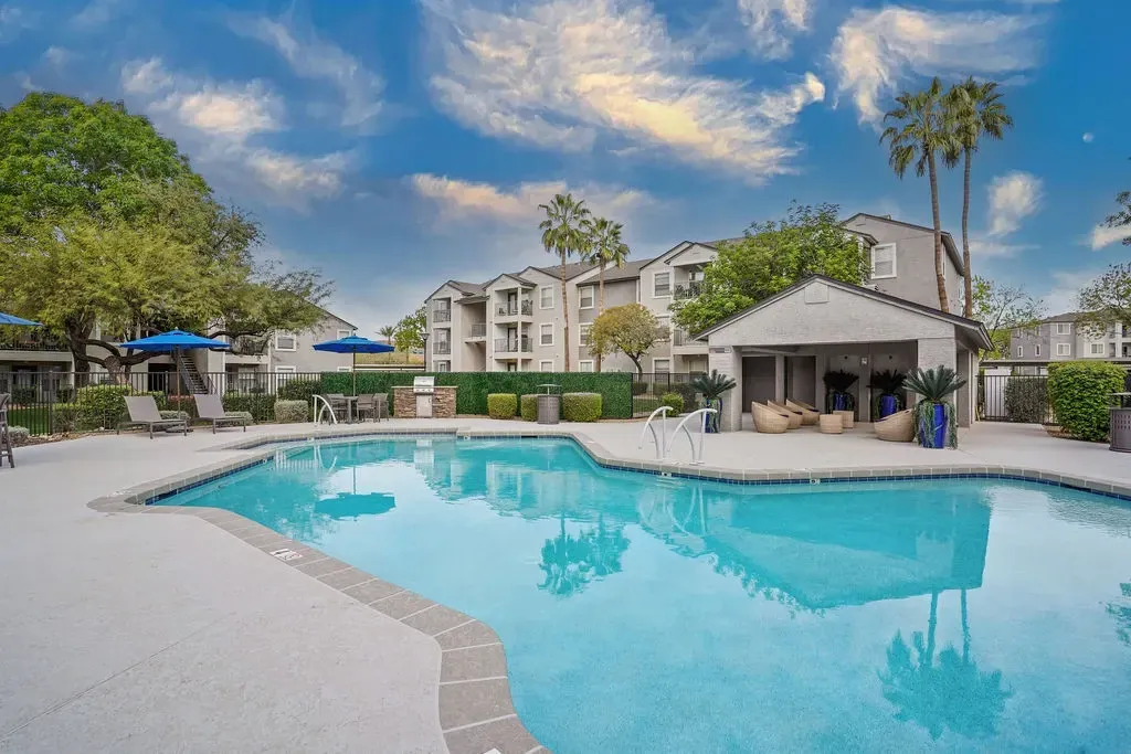 Outdoor pool at a multifamily community with lounge chairs, blue umbrellas, and a shaded cabana area.