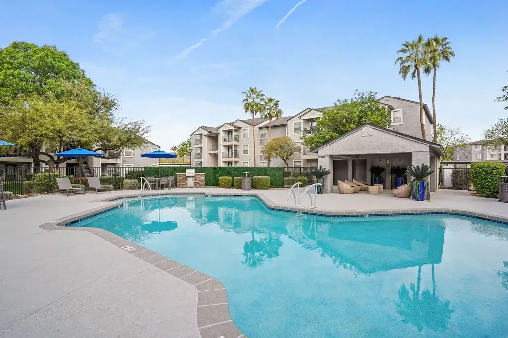 Outdoor apartment community pool with lounge chairs, umbrellas, and surrounding buildings.