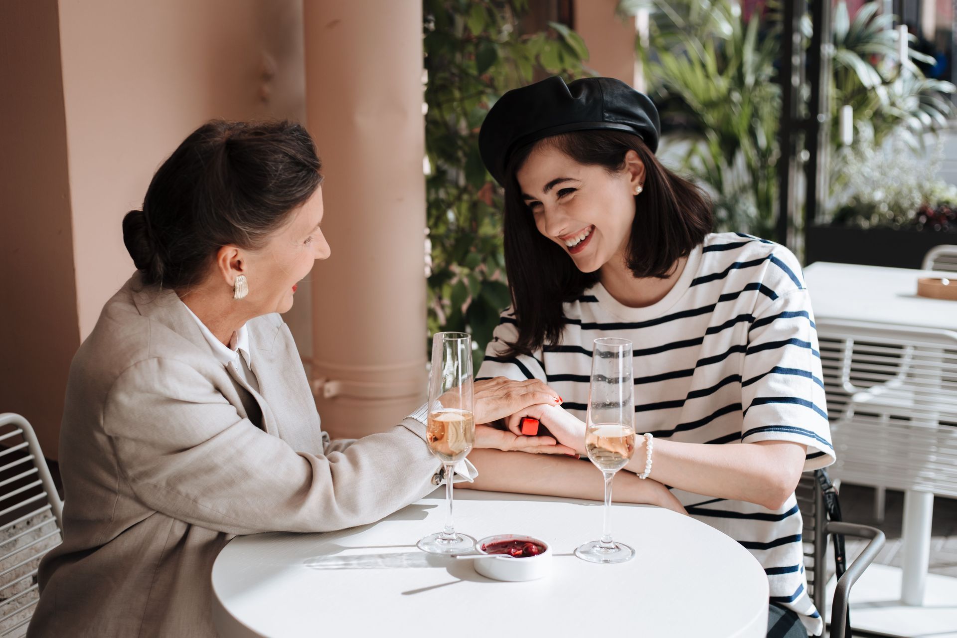 Two women chatting at a café table with drinks, one gesturing while the other smiles