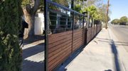 A modern wooden and metal fence alongside a sidewalk and road, with a partially visible person.