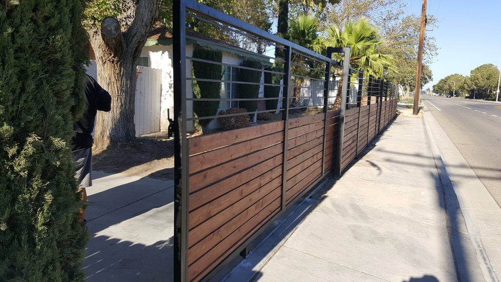 Modern wooden fence with black metal frame along a sidewalk next to a street.