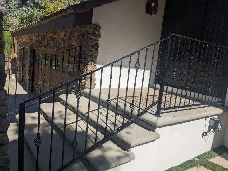 Outdoor concrete steps with black iron railing leading up to a building's entrance.