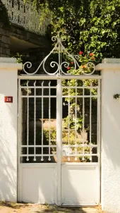 White wrought-iron gate with decorative top, leading to a garden, set in a white stucco wall.