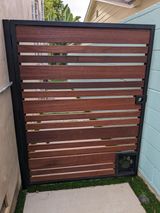 iron gate with horizontal slats, black frame, and a pet door with paw print, between walls.