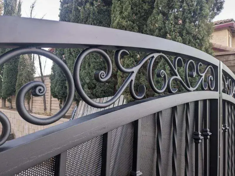 Black wrought iron gate with scrollwork details, arched top, and vertical bars and Ornamental iron work on it.