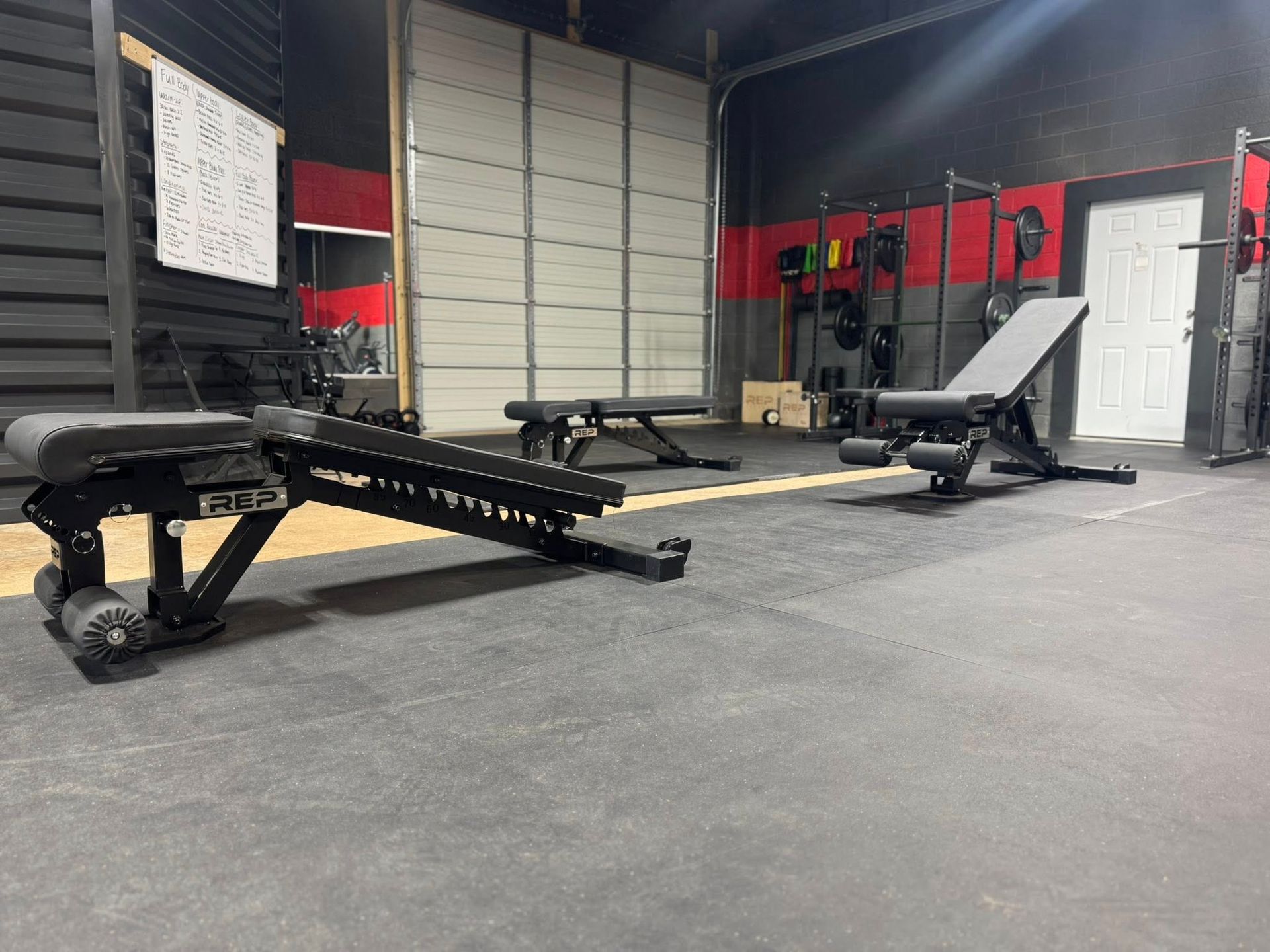 Gym interior with weight benches and equipment; black and red color scheme.