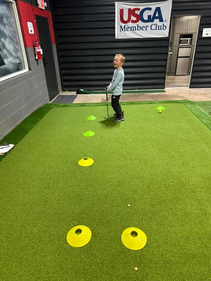 Young person putting golf ball on a green practice area with yellow cones.