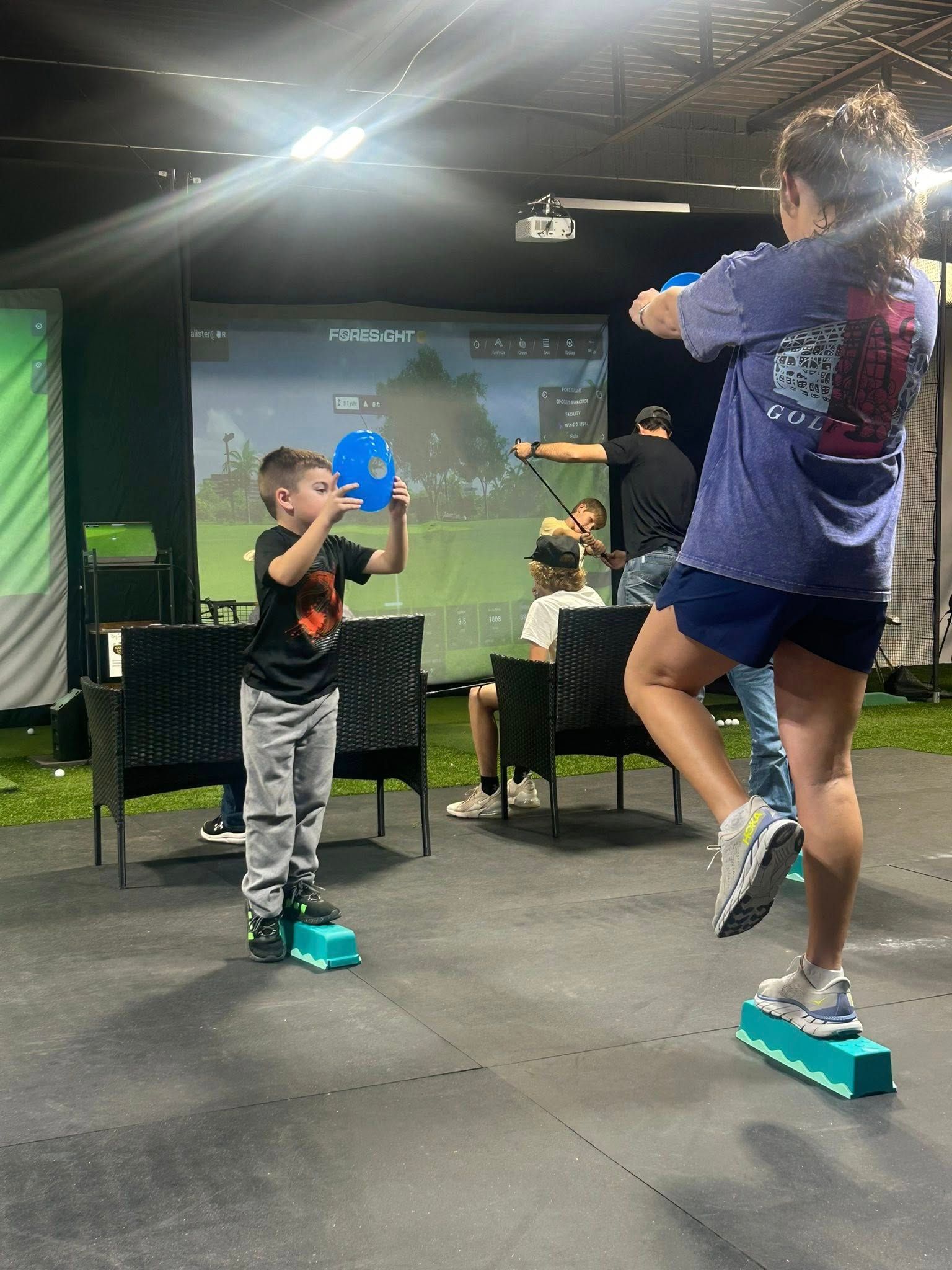 A child and an adult balance on blocks with balloons in a simulator room.