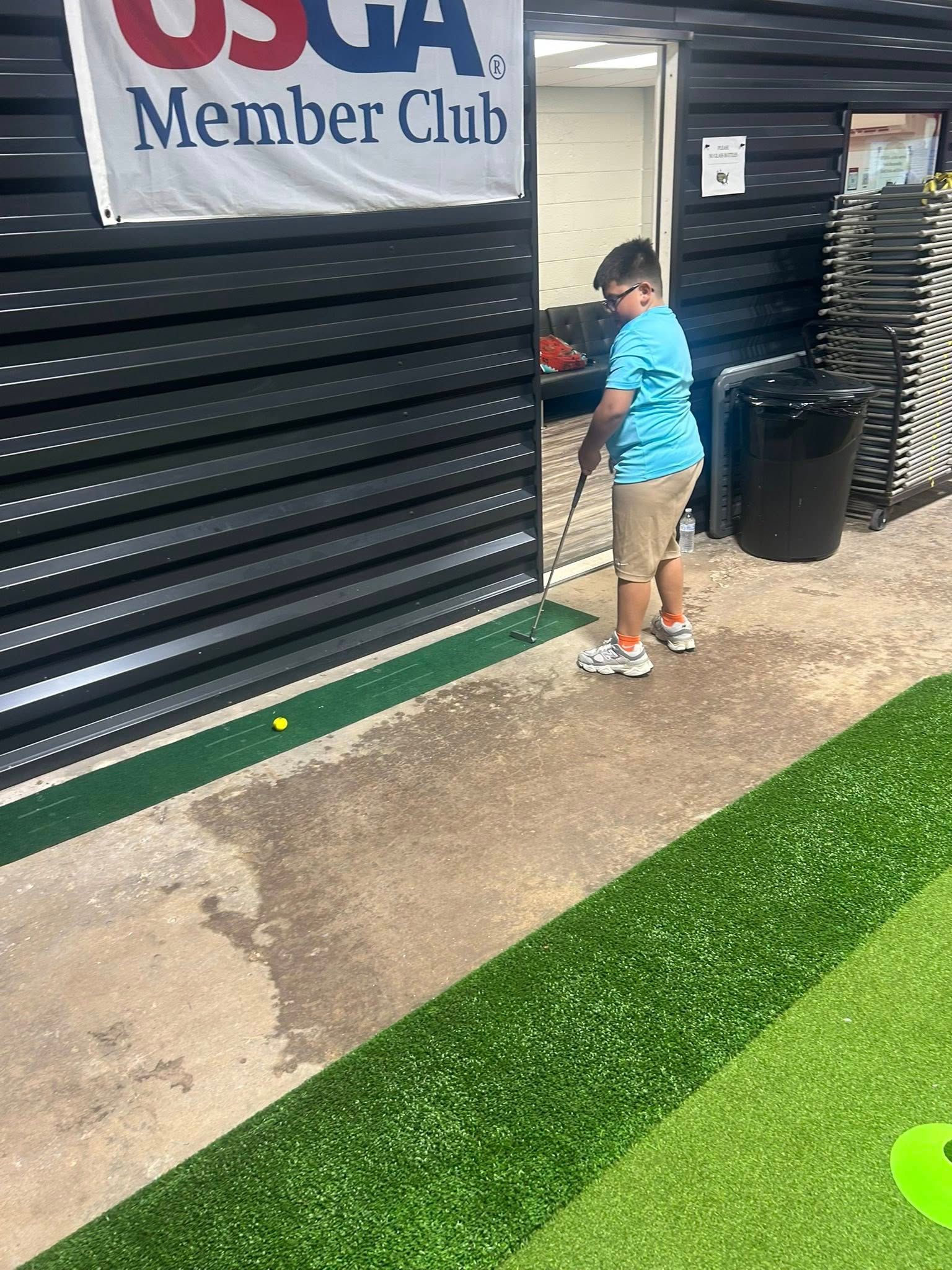 Boy in blue shirt playing golf, near a building marked 