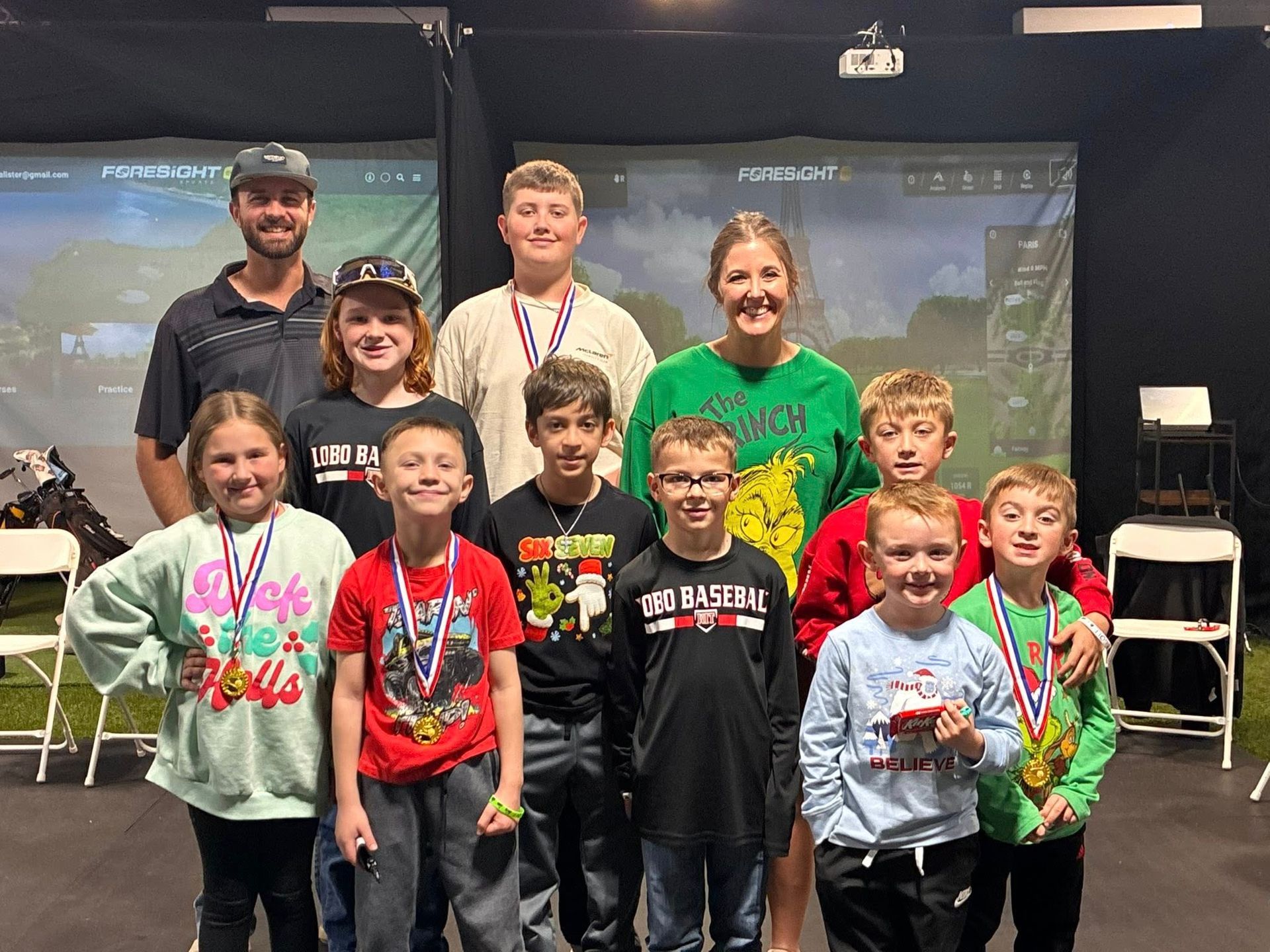Group of children and adults with medals, posing in front of a golf simulator backdrop.