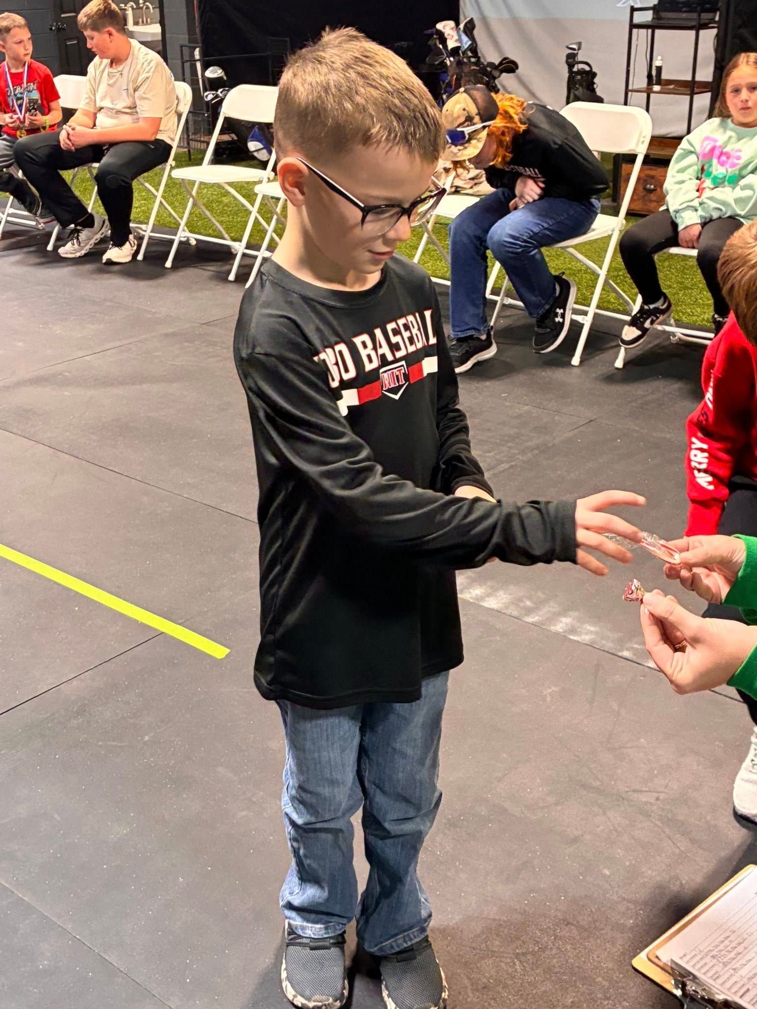 Boy in glasses holds something while another person's hand is near, indoors.