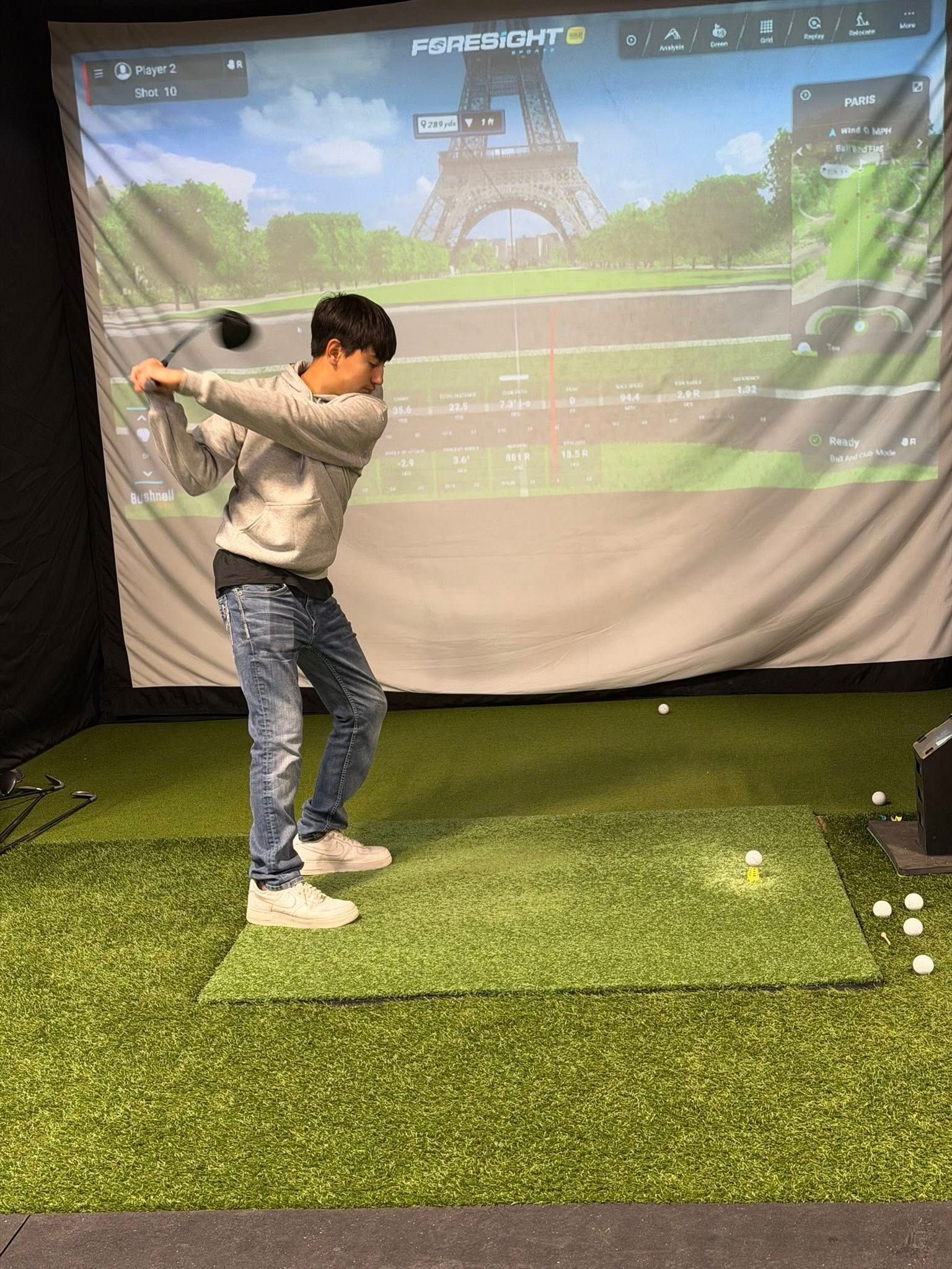 Person swinging a golf club in a simulator, Paris background.