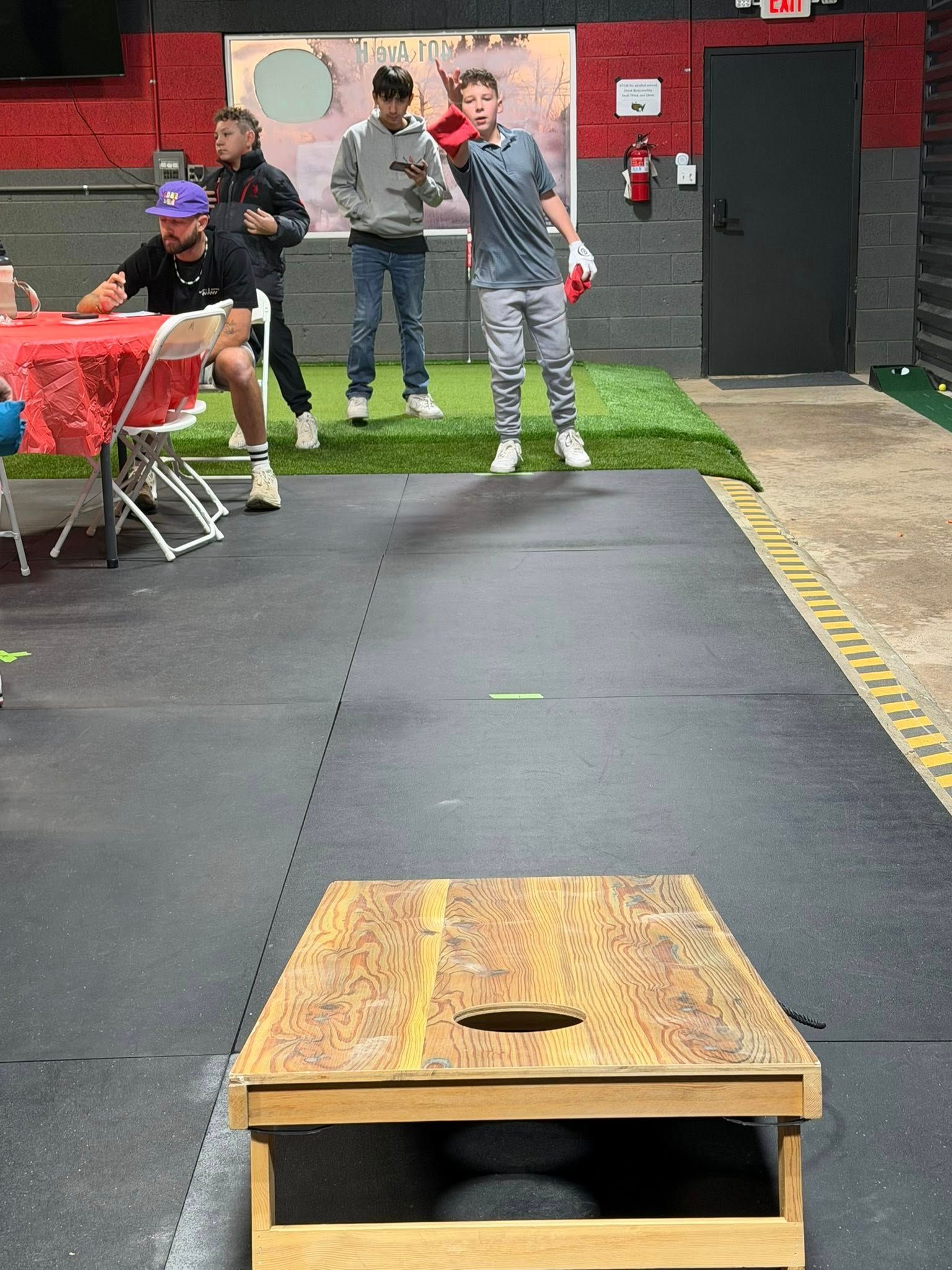 People playing cornhole indoors, with one person throwing a beanbag.