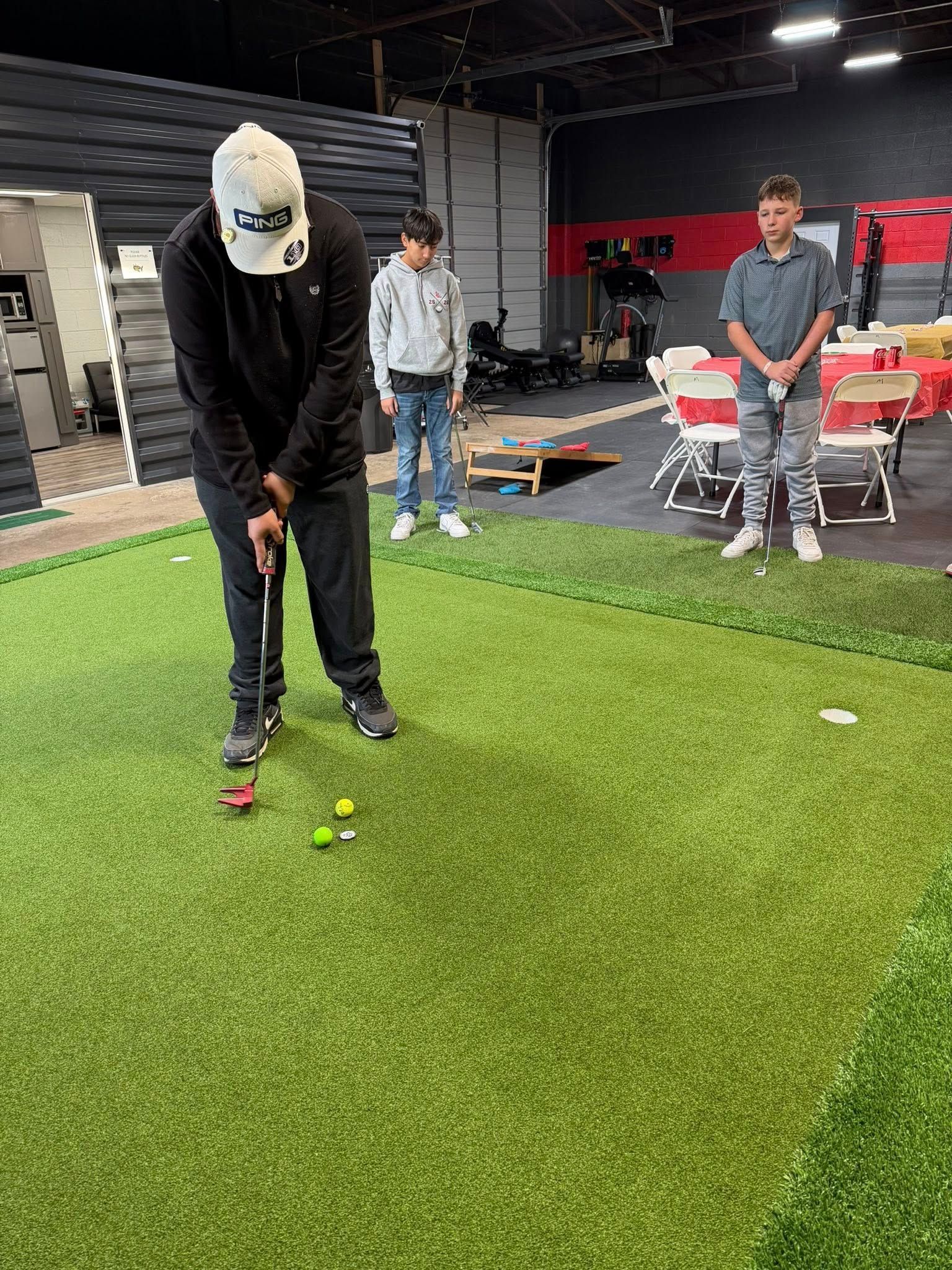 Man putting golf ball on a putting green; two people watch.