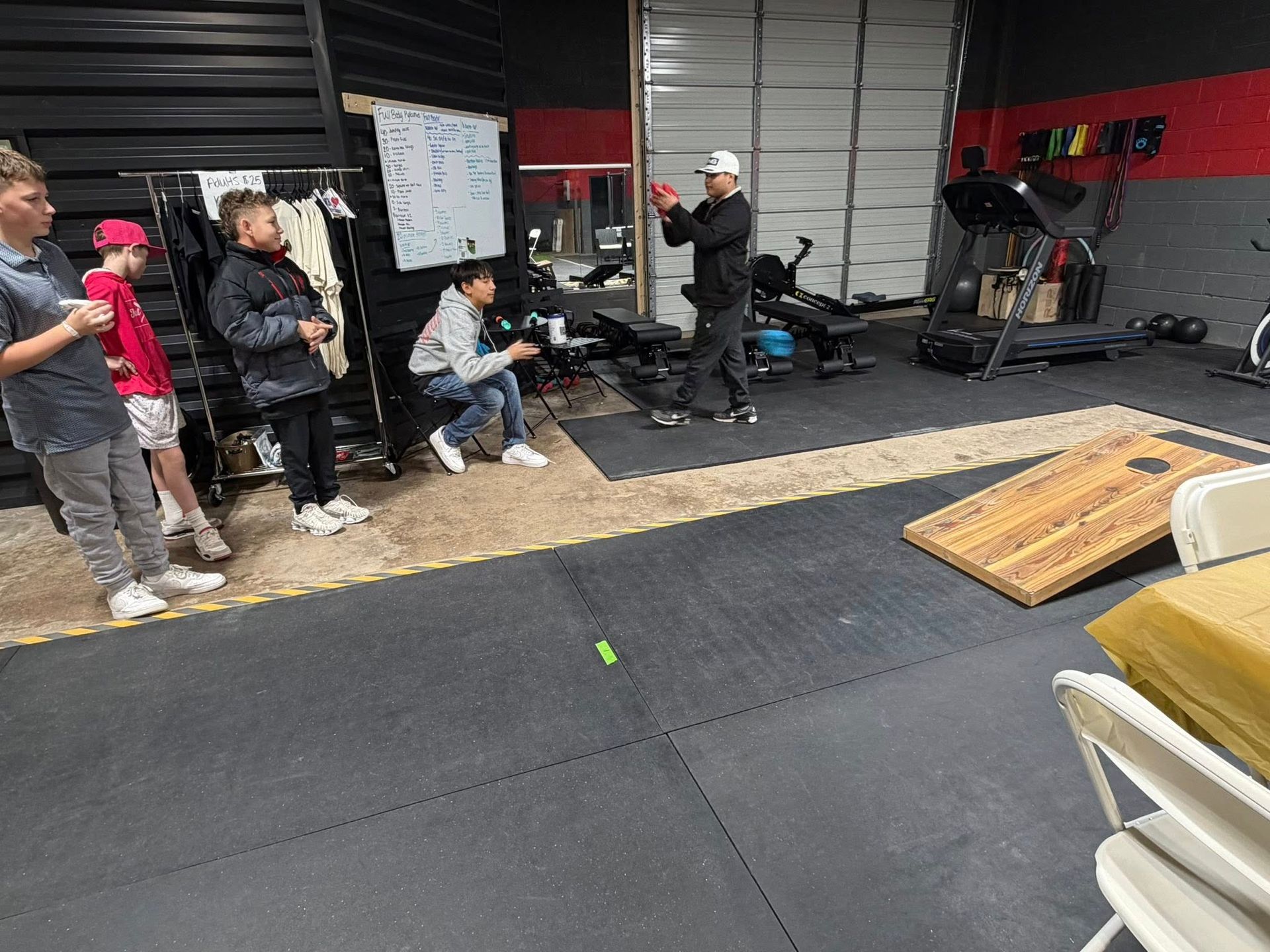 A group of people playing cornhole in a gym. One person throws a bean bag, others watch.