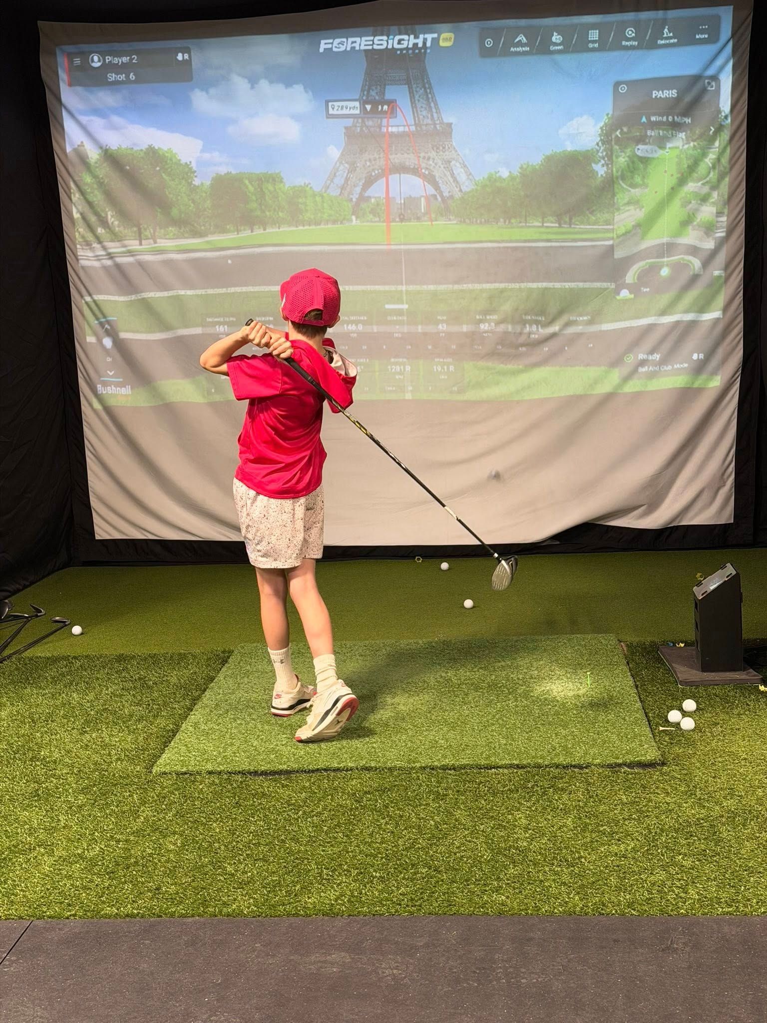 Person swings golf club at an indoor golf simulator; Paris background.
