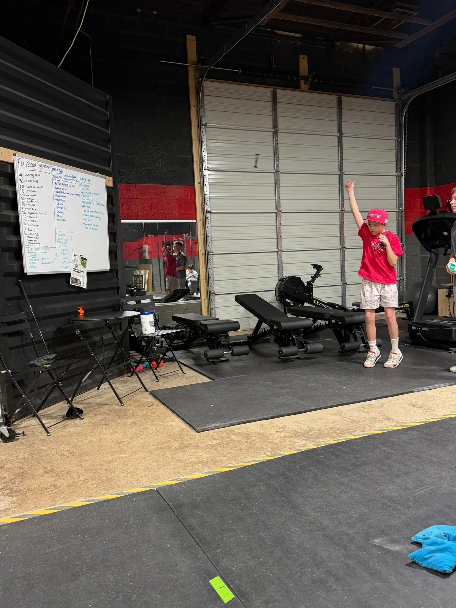 Person in a red shirt raises their arm in a gym, workout equipment in the background.