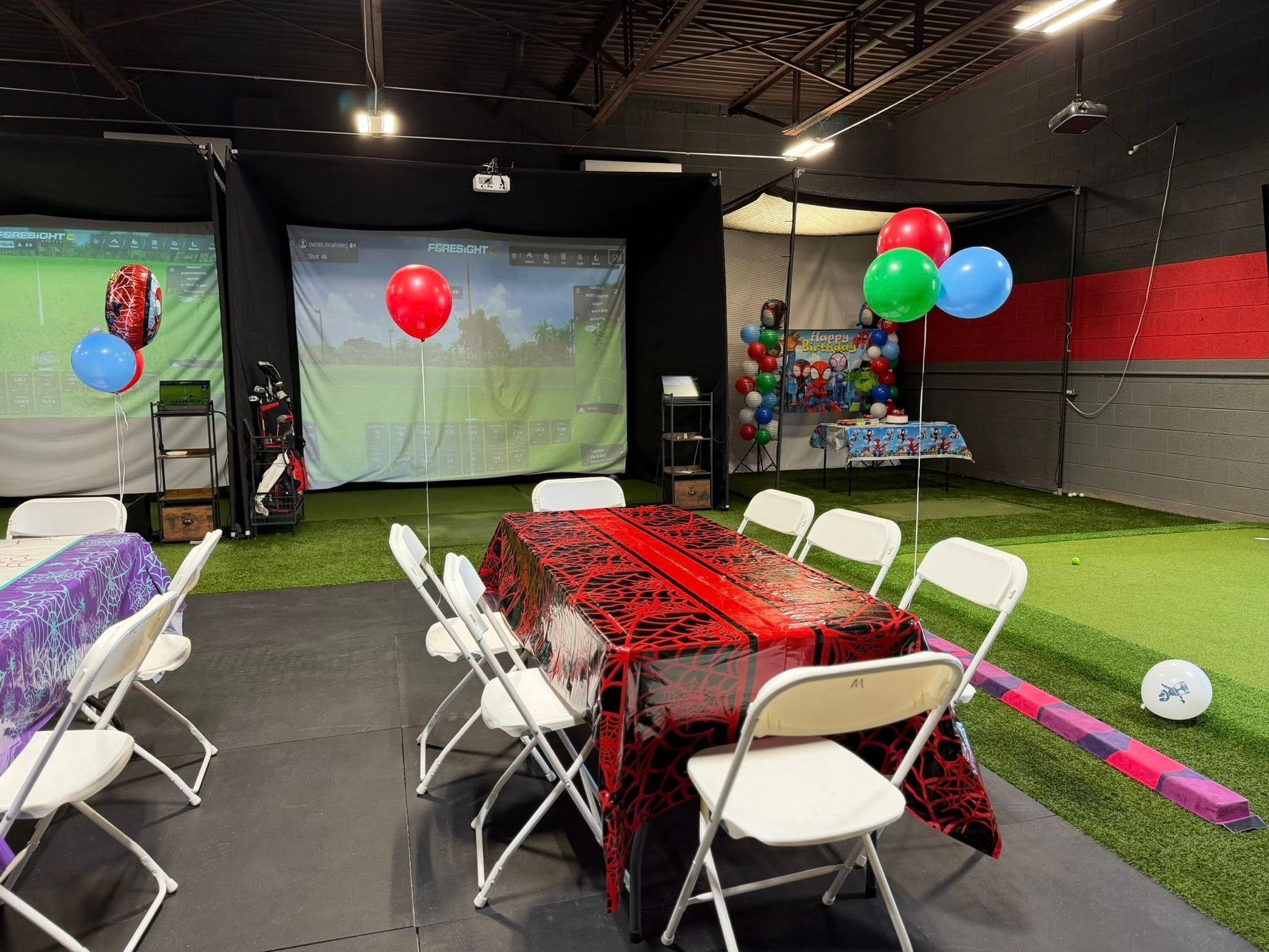 Party setup in indoor golf simulator area with tables, chairs, and balloons.