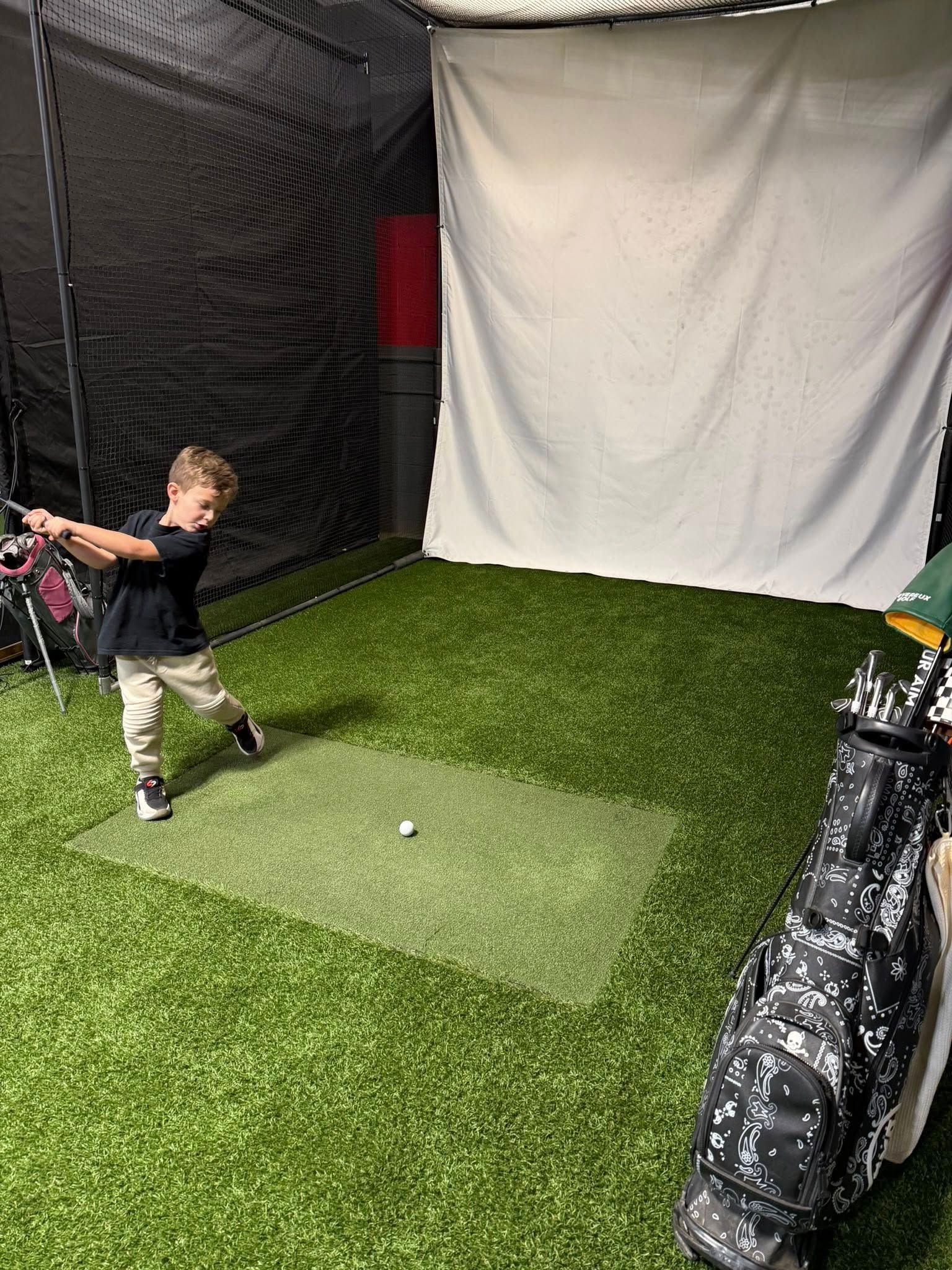 Child swinging a golf club in an indoor golf simulator. They are wearing casual clothes.