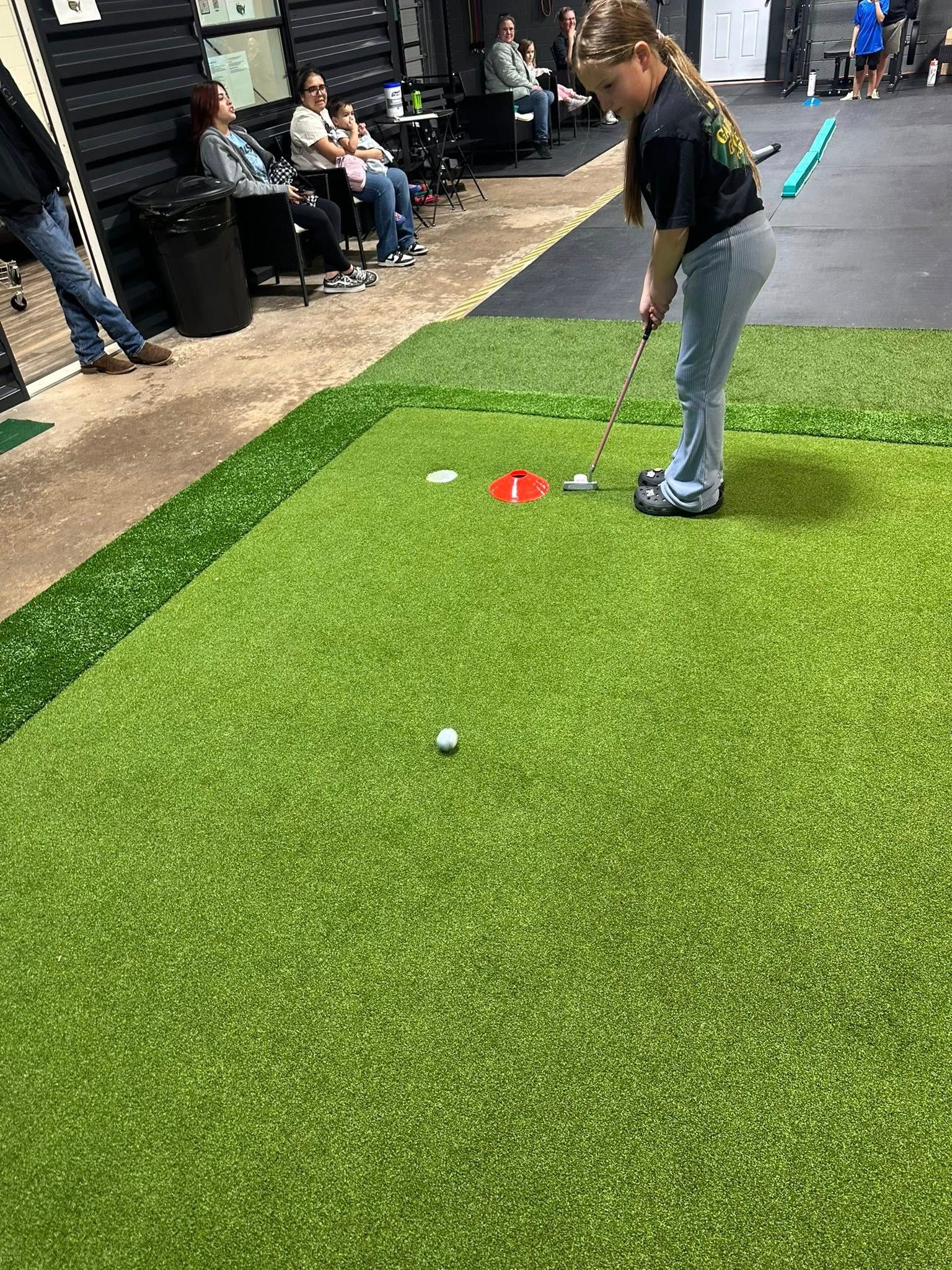 Woman putting a golf ball on a green, other people in the background.