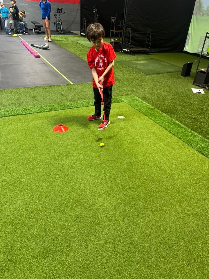 Boy in red shirt putting golf ball on a mini-golf course.
