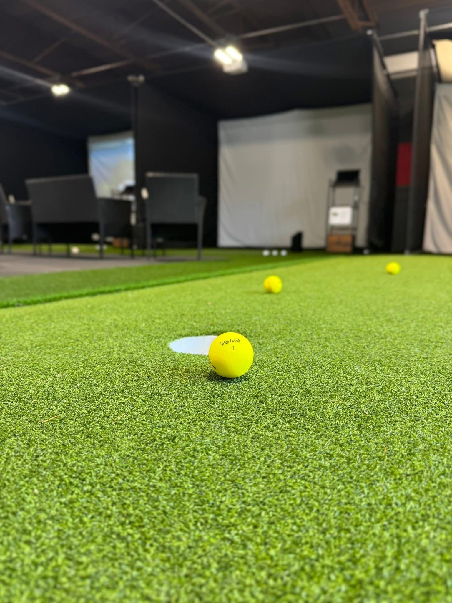 Yellow golf ball near the hole on a green putting surface, indoor golf setting.