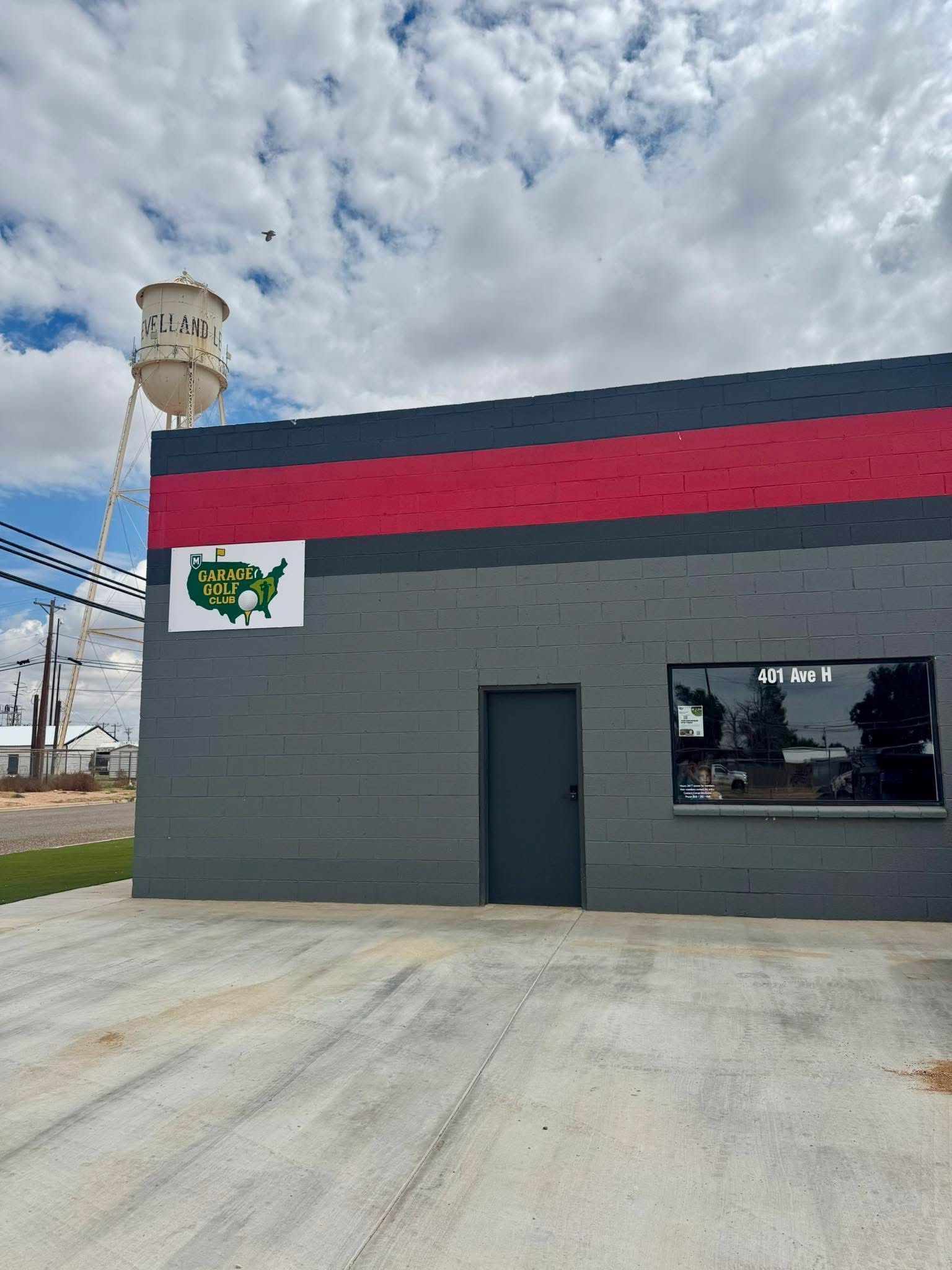 Gray and red building with a logo, water tower in background under cloudy sky.