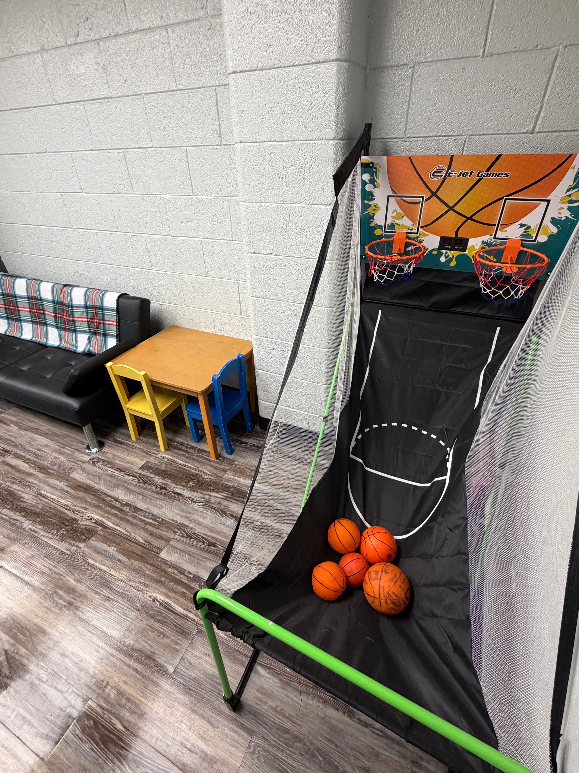 Basketball arcade game with orange balls, a table, and a small couch.